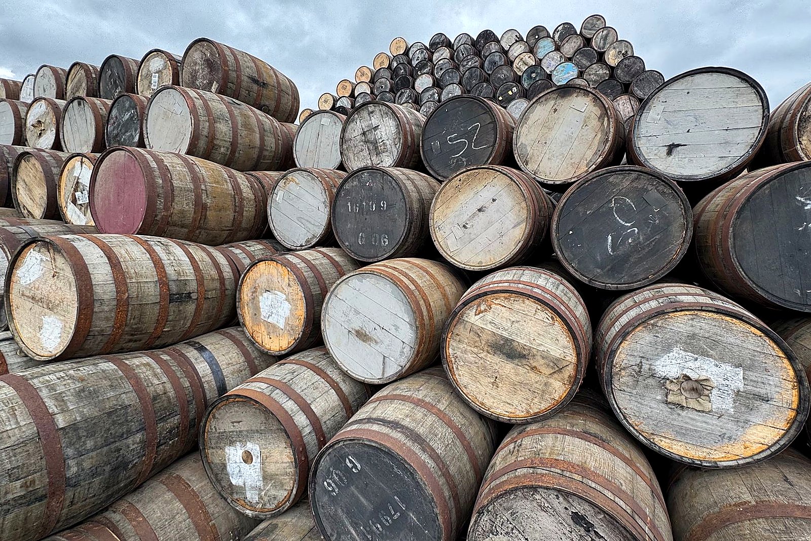Stacked weathered oak barrels outdoors under soft Maine sky.