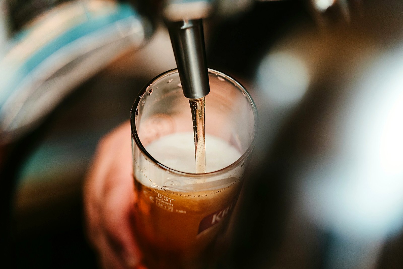 Close-up of amber beer pouring from a tap into a tall glass with foam.