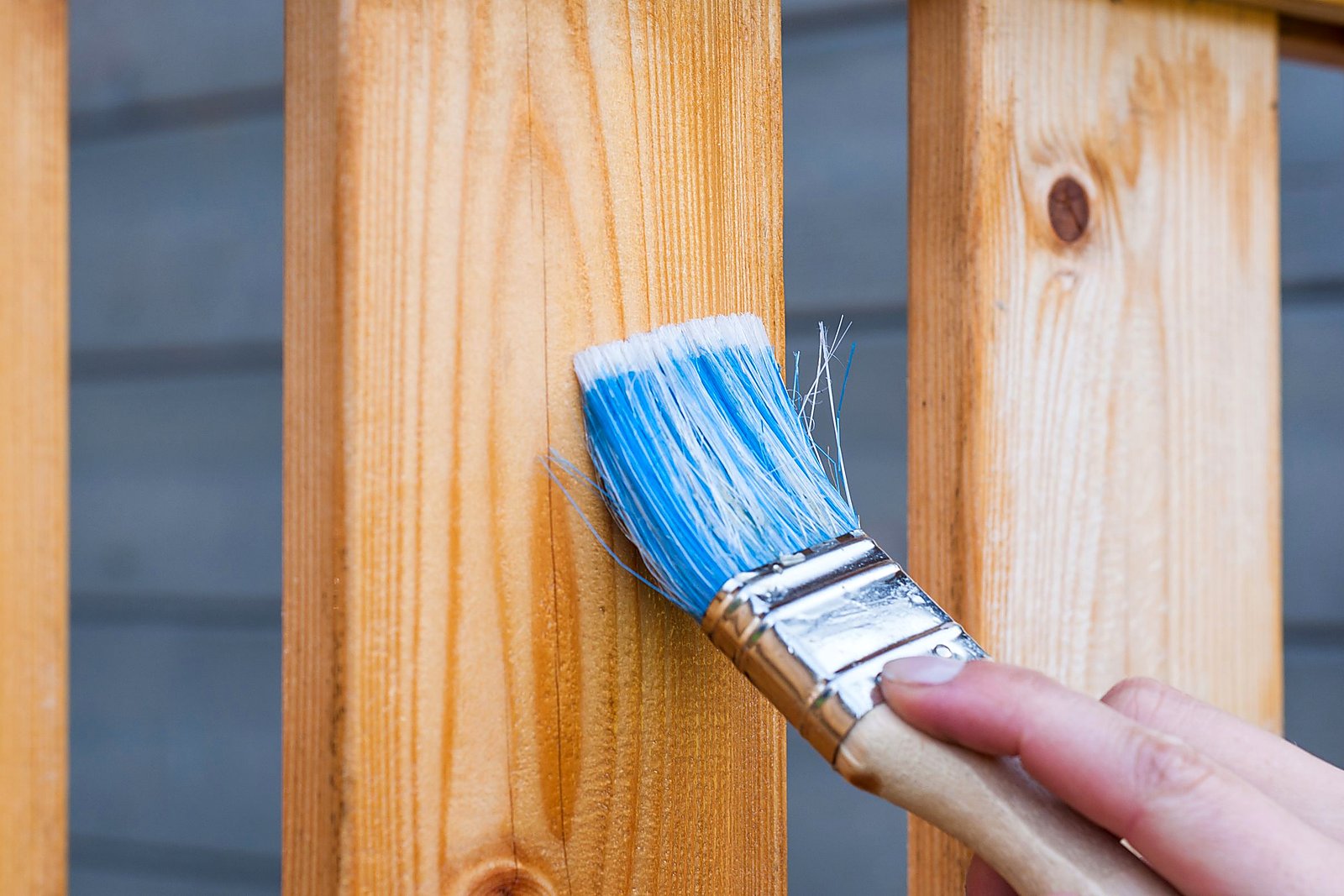Hand brushing finish onto fresh vertical wood siding in bright daylight.