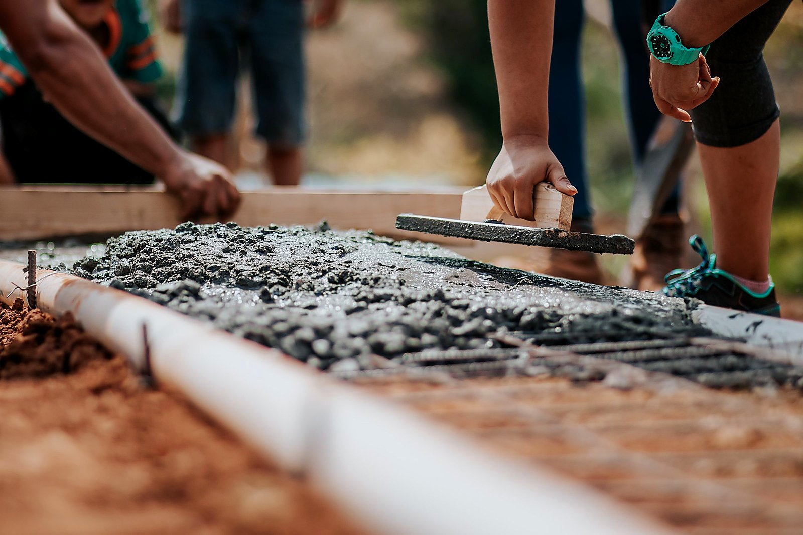 Worker leveling wet concrete foundation with a hand float over rebar.