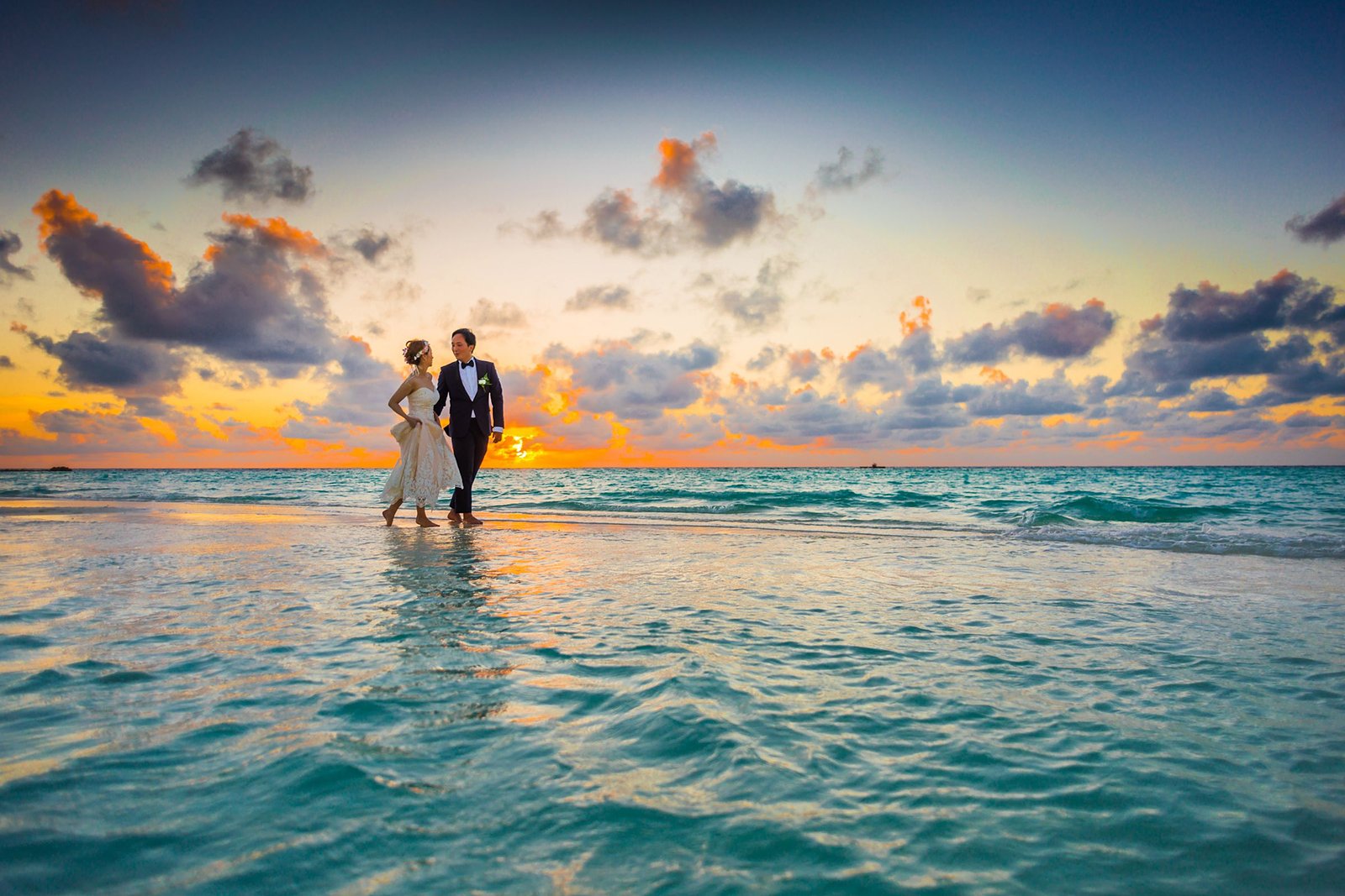 Couple walking the shoreline at sunset — grounds reveal.