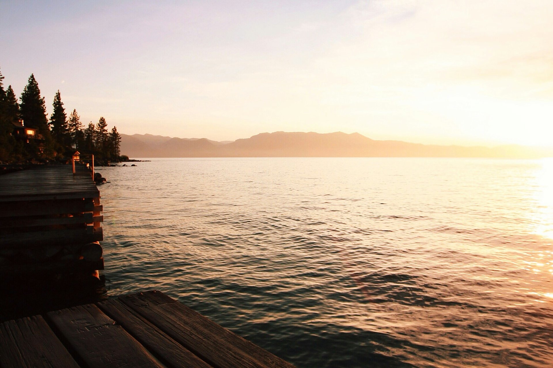 Wooden dock at golden hour on a still lake, sun shimmering on the water.