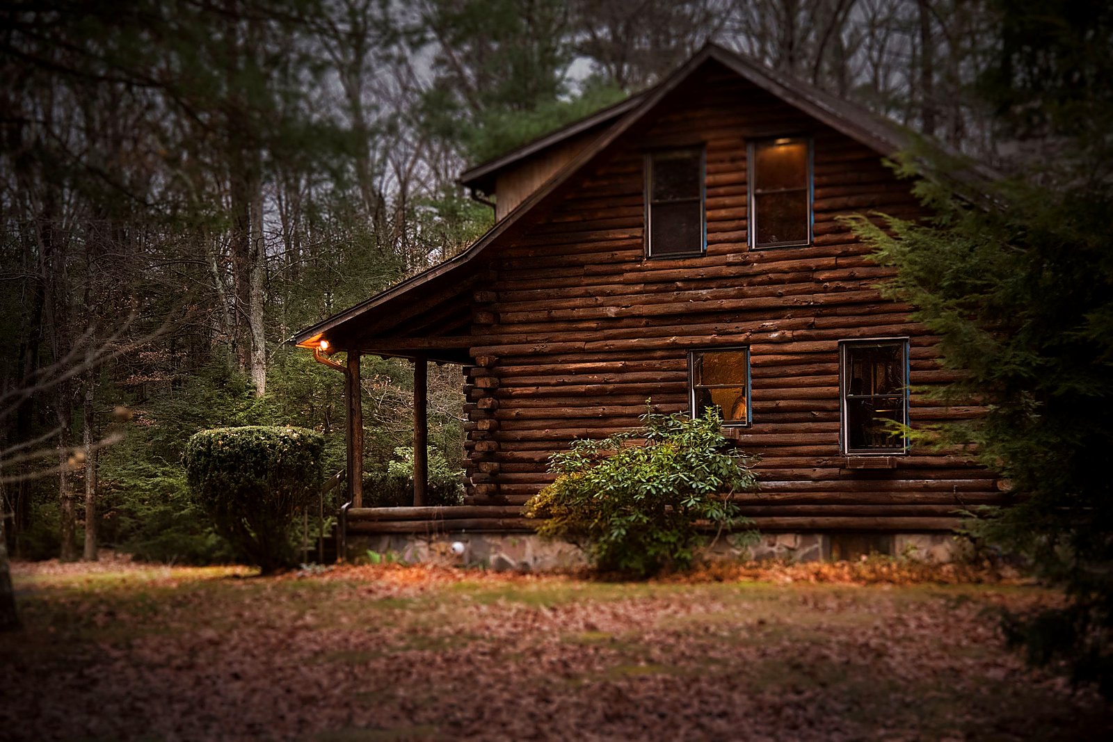 Warm porch light glowing on a log inn at dusk among autumn leaves.