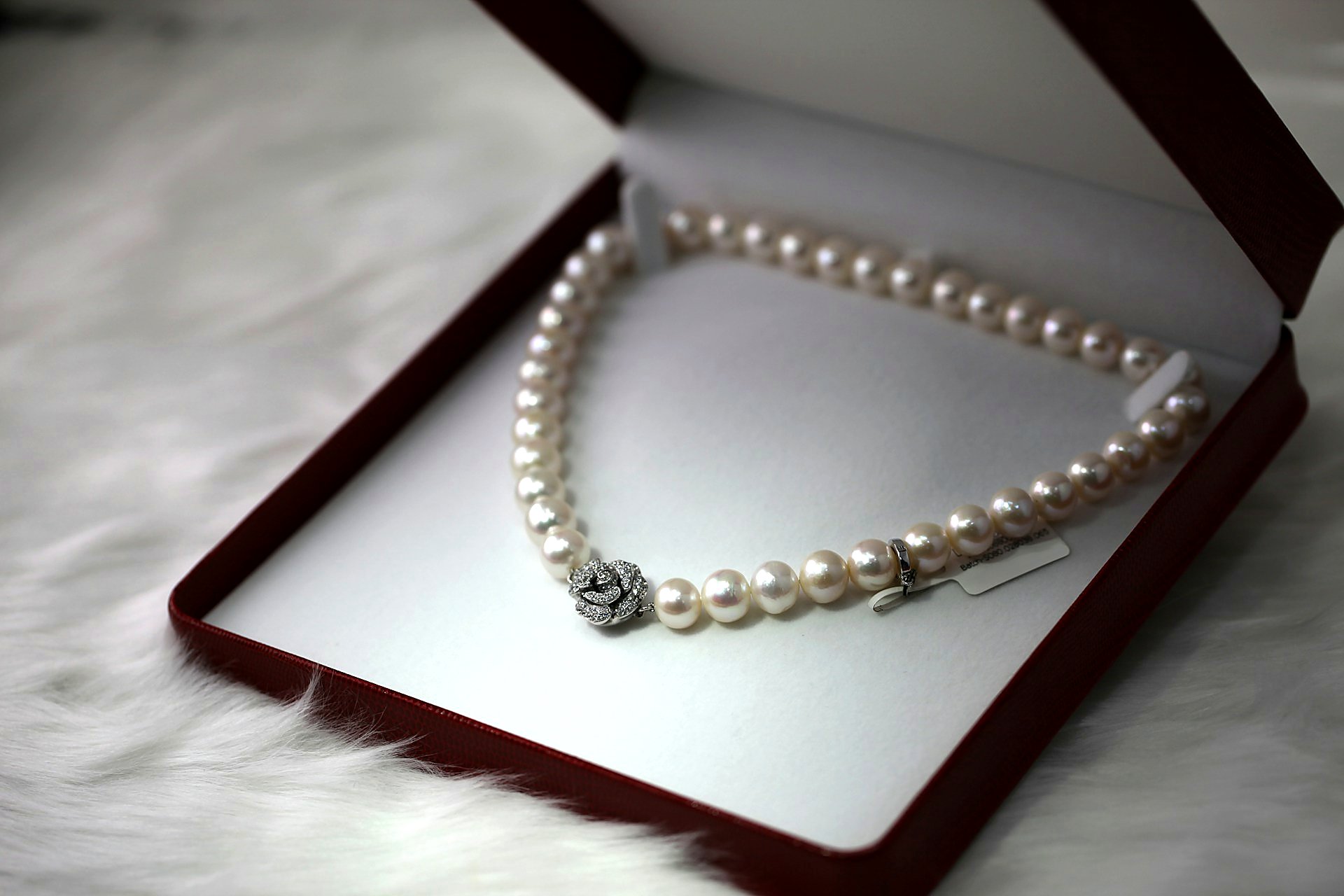 Cream pearl strand with diamond rose clasp in an open red jewelry box.