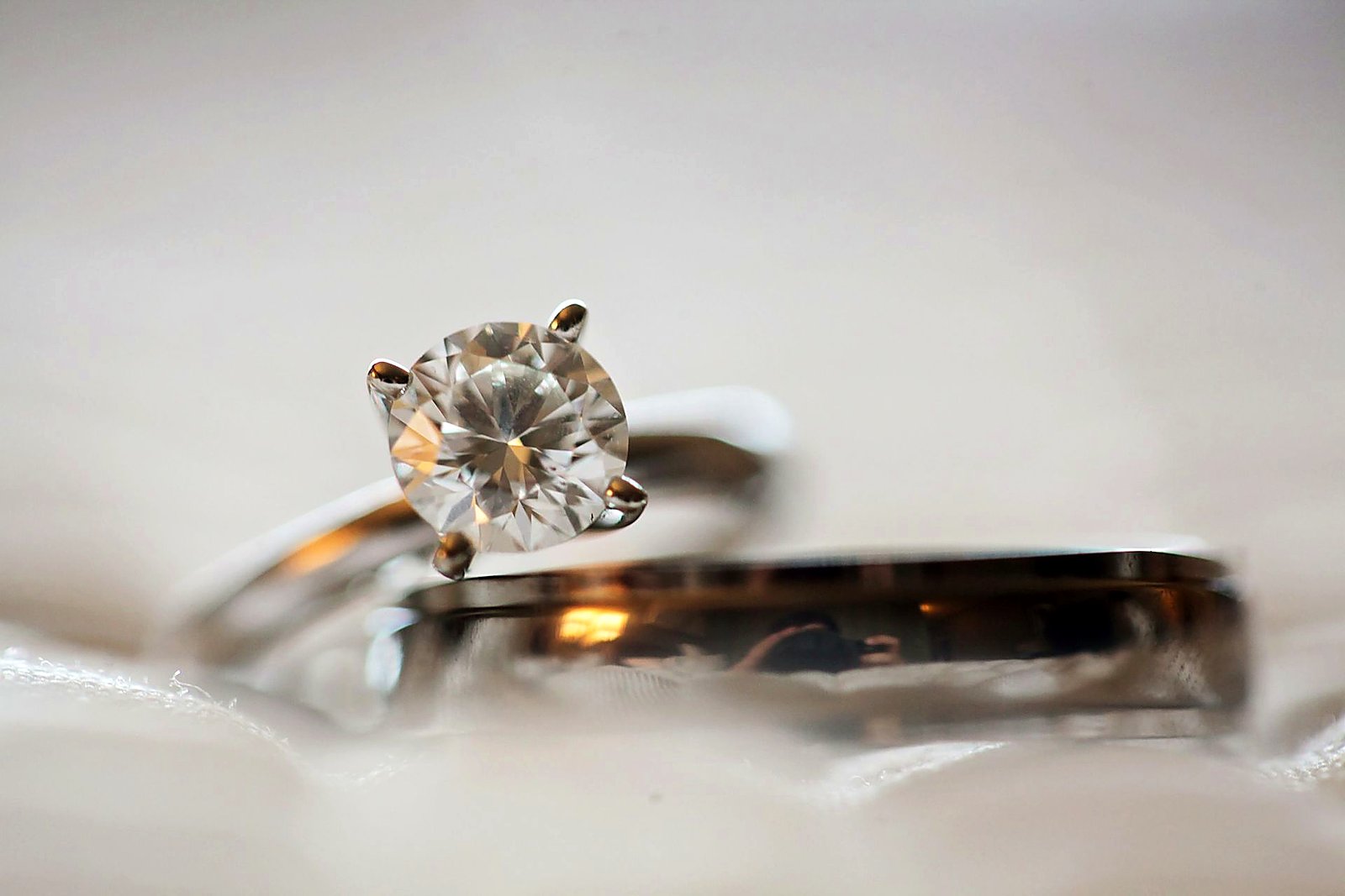 Classic diamond solitaire and polished wedding band on soft white cloth.