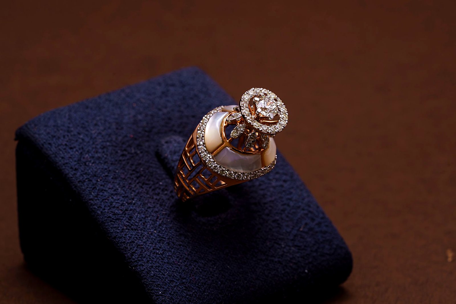 Ornate gold diamond and pearl ring displayed on a dark velvet stand.