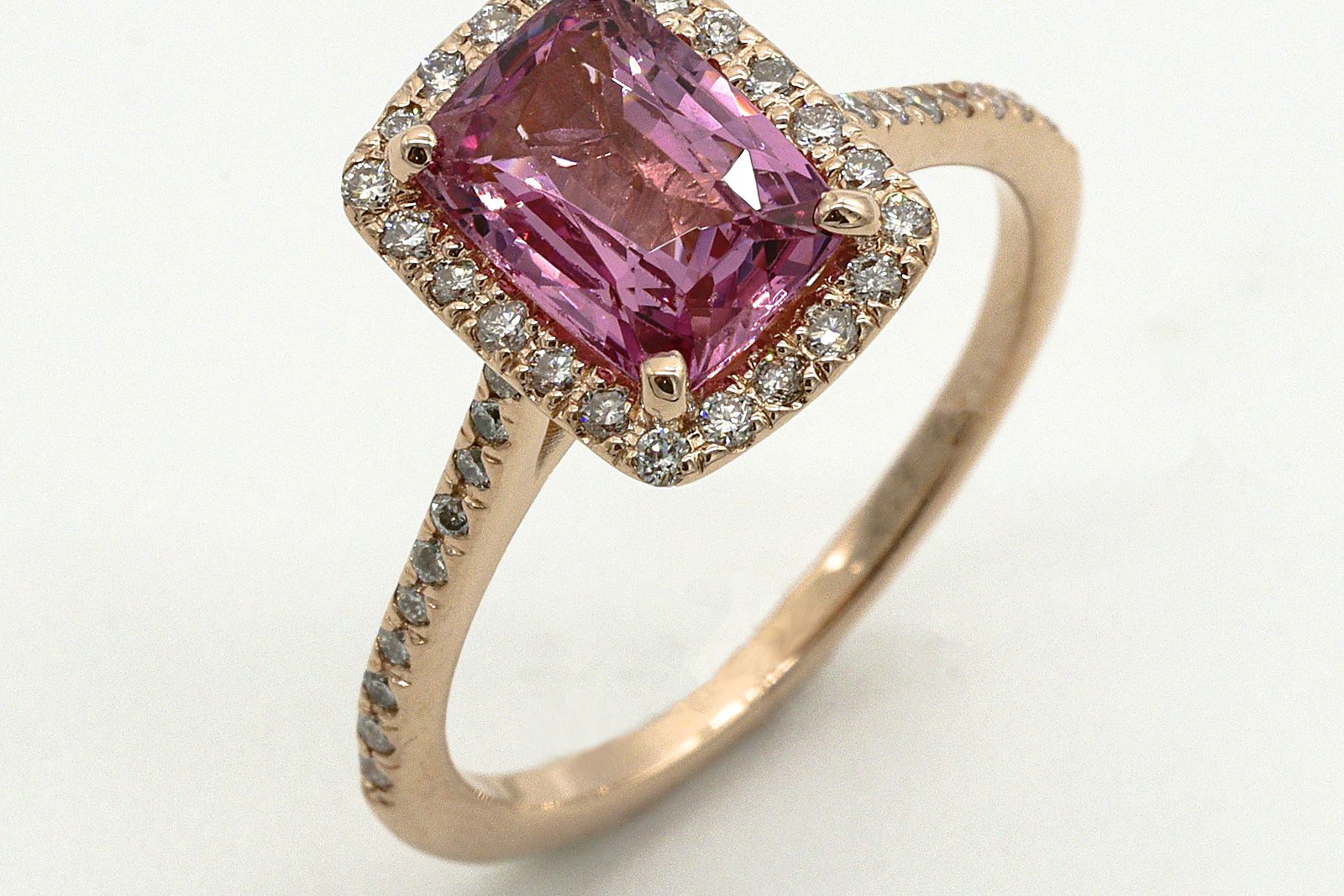 Pink gemstone halo ring in rose gold on a light surface.